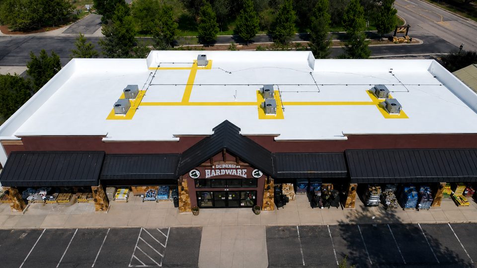 After: the same Durango hardware store roof coated bright white with a Conklin reflective system and yellow marked service walkways