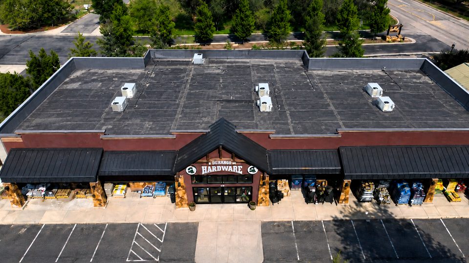 Before: aerial view of a retail hardware store's aging dark flat roof with weathered seams and rooftop HVAC units in Durango, Colorado