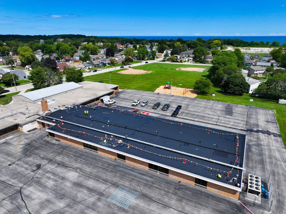 Before: aerial view of a school's dark flat roof being prepped by the crew ahead of a silicone roof coating