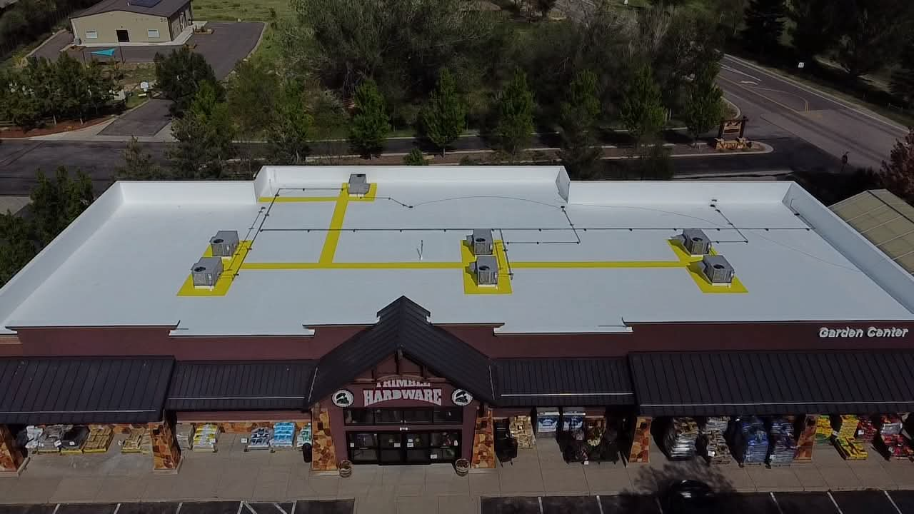 After: the same hardware store roof coated bright white with a Conklin reflective system and yellow marked service walkways